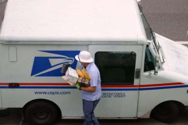 United States Postal Service USPS mailman wears a mask and gloves while carrying a load of parcels from a mail truck during the COVID-19 coro<em></em>navirus pandemic.